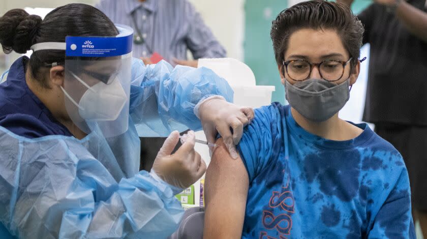 Eagle Rock, CA - August 30: Registered Nurse Priscilla V., left, gives a Pfizer-BioNTech vaccine shot to Dean Iida, 17, a senior at Eagle Rock High School, as Los Angeles County Board of Supervisors Chair Hilda Solis, Interim Superintendent Megan K. Reilly, School Board members Kelly Gonez and Jackie Goldberg and special guests visit Los Angeles Unified School-based mobile vaccination clinics at Eagle Rock High School on Monday, Aug. 30, 2021 in Eagle Rock, CA. All employees in the Los Angeles Unified School District must be vaccinated against COVID-19 by Oct. 15, an order that puts it at the forefront of school systems across the country that are mandating strict coronavirus safety measures for employees and students. (Allen J. Schaben / Los Angeles Times)