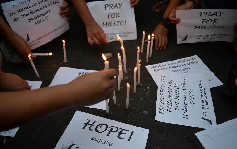 Students light candles as they hold placards in solidarity with families of the passengers of the missing Malaysia Airlines flight MH370 plane during a candle light vigil at the university belt in Manila on March 13, 2014