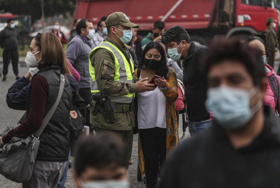 Un oficial de policía verifica los permisos de tránsito de las personas el jueves 1 de abril de 2021 en medio de una cuarentena por la pandemia de coronavirus afuera del Mercado Central, donde los compradores aguardan a comprar pescado para la Semana Santa, en Santiago, Chile. (AP Foto/Esteban Félix)