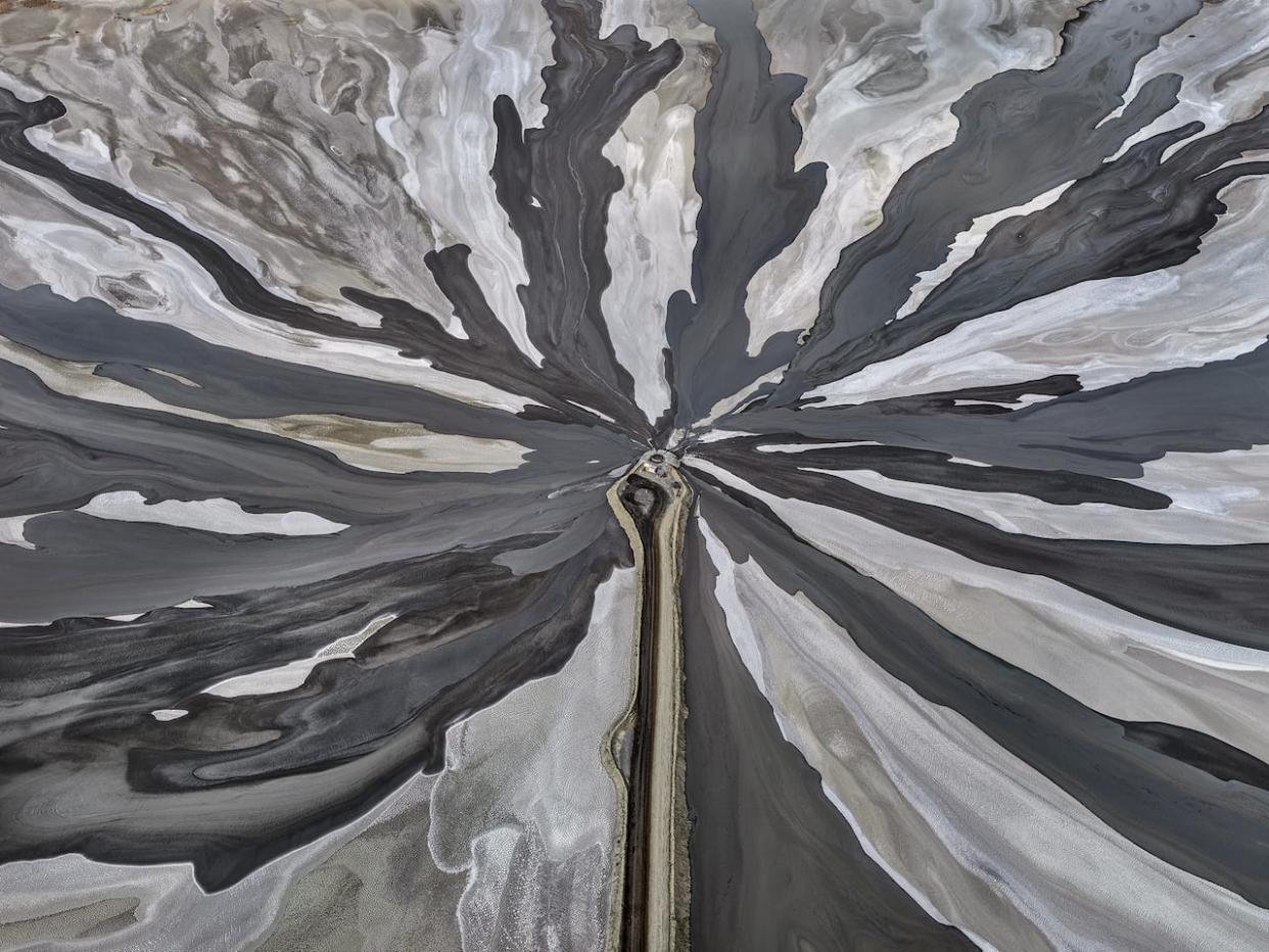 This photograph, taken by Edward Burtynsky in 2018, showcases a tailings pond at the Wesselton Diamond Mine in Kimberley, South Africa, nicknamed 'Diamond City.' The conveyor belt featured in the centre is guiding the kimberlite tailings (waste material from diamond mining) into a waste pond. (© Edward Burtynsky, courtesy Flowers Gallery, London - image credit)