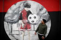 Roberto Mensi, the leader of the Autoconvocados Newells fans group, poses for a photo standing next to a mural depicting a young Lionel Messi, at a soccer field used by the Newell's Old Boys youth teams, Messi's childhood soccer club, in Rosario, Argentina, Thursday, Aug. 27, 2020. Newell's Old Boys' fans hope to lure him home following his announcement that he wants to leave Barcelona F.C. after nearly two decades with the Spanish club. (AP Photo/Natacha Pisarenko)