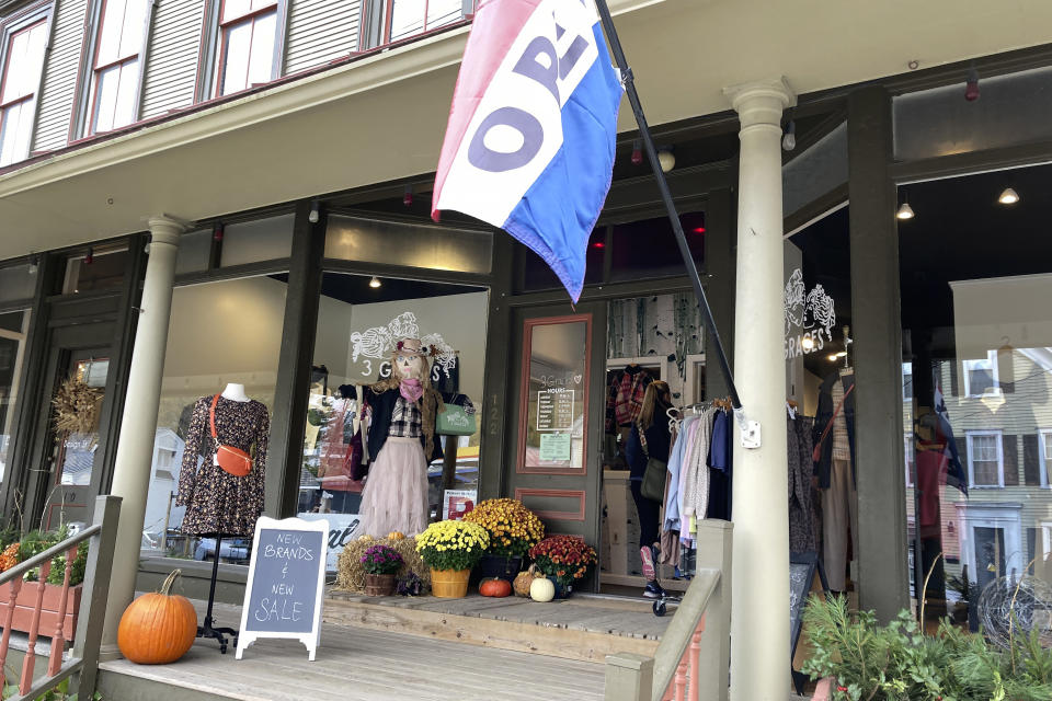 An "open" flag hangs outside an entrance to a clothing and accessories shop, Thursday, Oct. 19, 2023, in Ludlow, Vt., three months after severe flooding hit the ski town. As winter approaches and the fall tourism season lingers, Ludlow businesses who lost out on summer tourism want to get the word out that they are open, even though a handful are still in the throes of rebuilding. (AP Photo/Lisa Rathke)