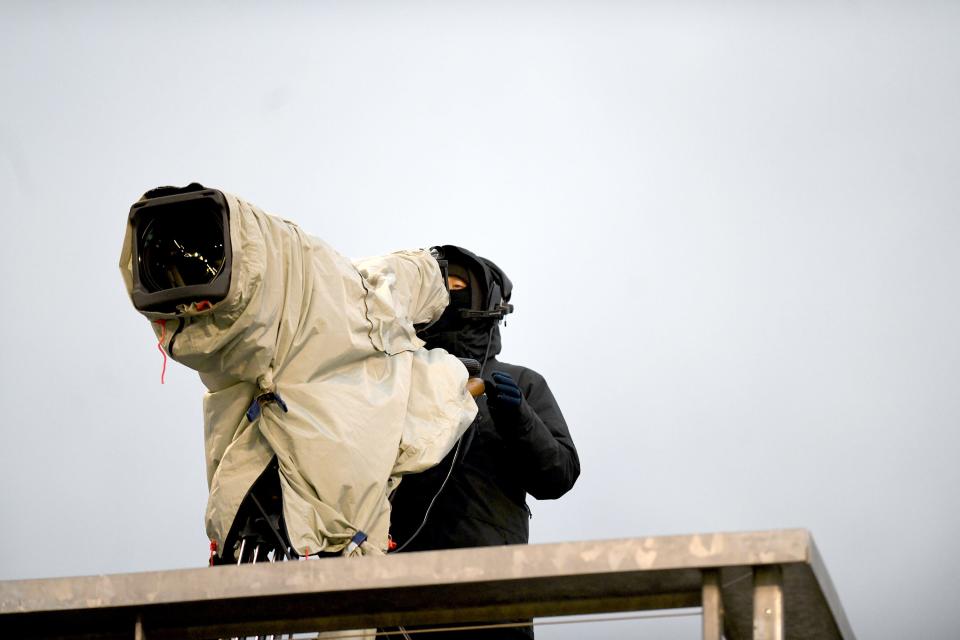 A cameraman covers up against the weather during the OHSAA State Football Championships at Tom Benson Hall of Fame Stadium in Canton.