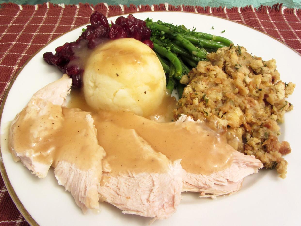 Photo of white meat turkey with mashed potatoes, gravy, cranberry sauce, green beans and stuffing served for thanksgiving.