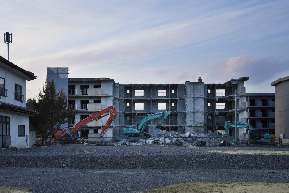 Heavy-duty machines sit unmanned in the evening by a building that looks getting torn down in Futaba town, northeastern Japan, Wednesday, March 2, 2022. Most damaged buildings have been torn down in the last 11 years. (AP Photo/Hiro Komae)