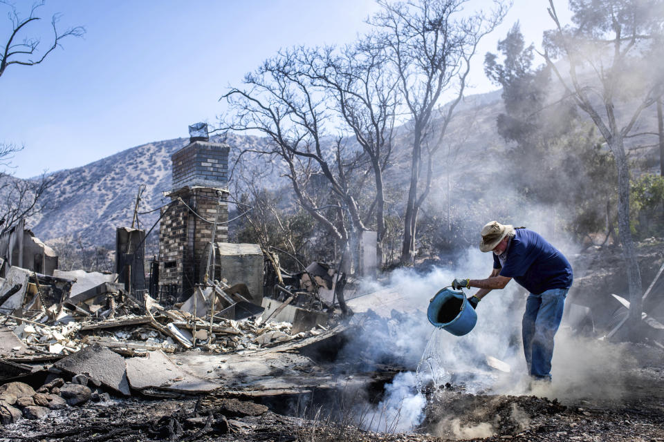 Dale Burton, of Leona Valley, tries to put out the fire that continues to smolder at his friend Cheryl Poindexter's property on Monday, Sept. 21, 2020 after the Bobcat fire burned her home of 27 years and the 11 acre property where she ran an animal rescue in Juniper Hills, Calif. (Sarah Reingewirtz/The Orange County Register via AP)
