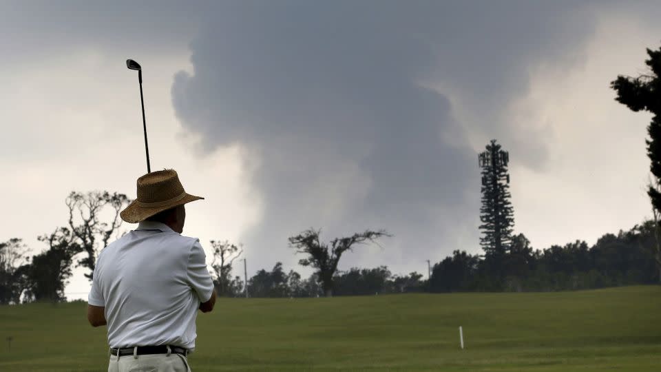 A golfer plays the Volcano Course as ash from the summit crater of Kilauea rises in the background, May 2018. - Caleb Jones/AP