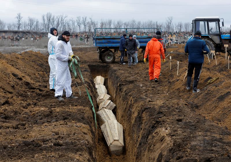 FILE PHOTO: Workers lower coffins into a common grave during a burial at a cemetery outside Mariupol