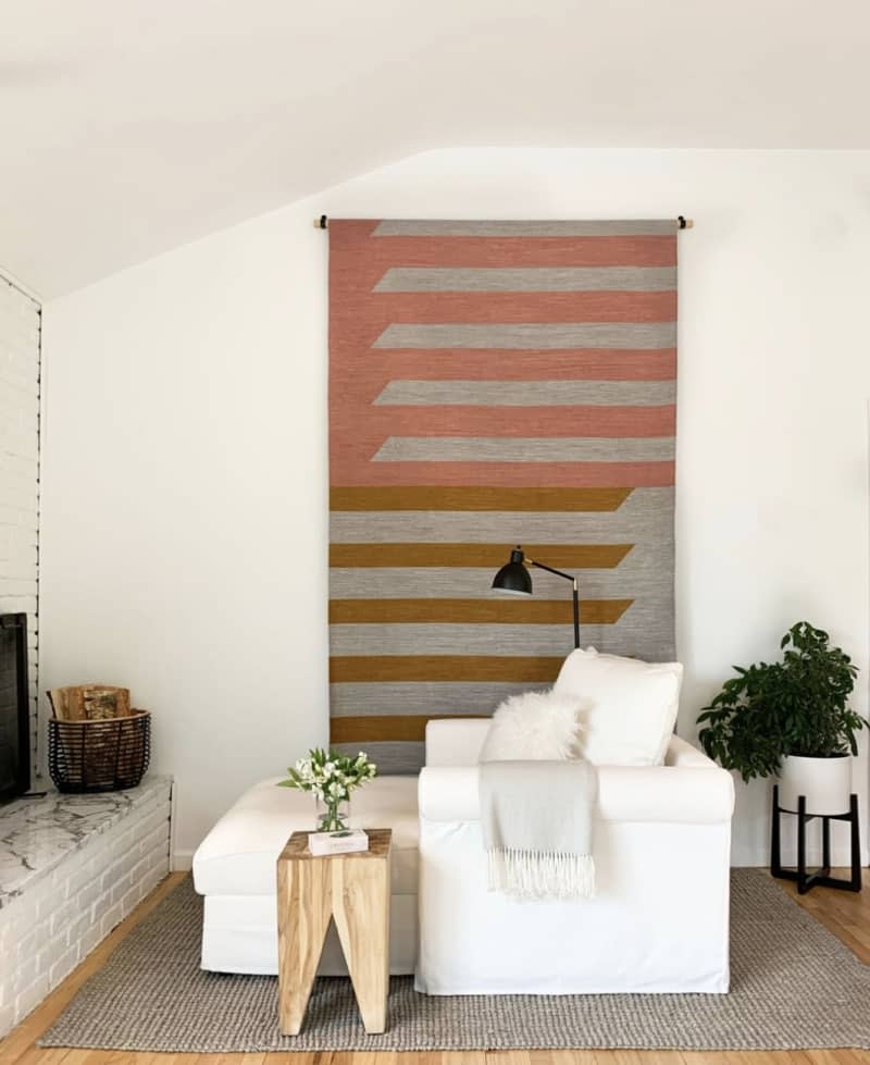 A living room with a pink, grey, and ocher striped rug hung on the wall