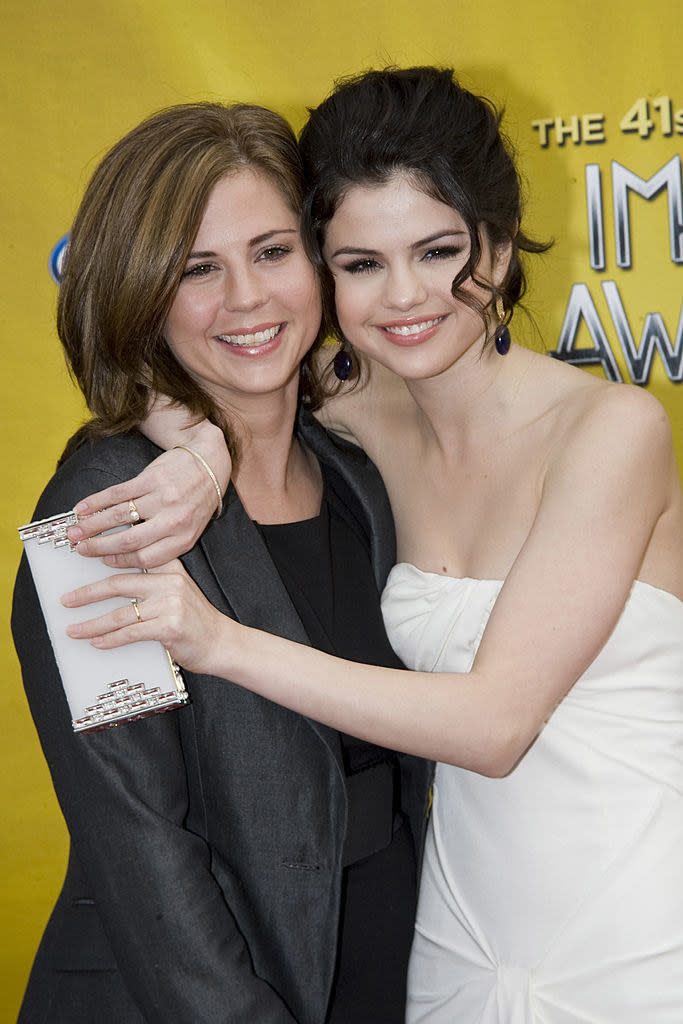 Smiling Selena, wearing a strapless outfit, hugs her smiling mother