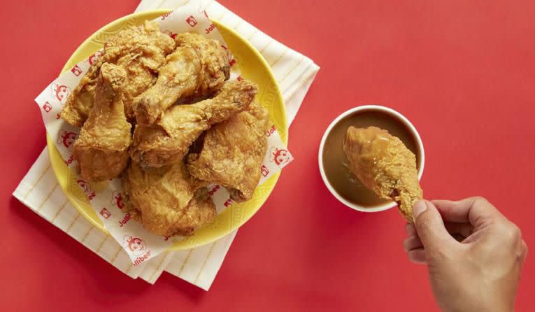 bucket of jollibee chicken with one tender getting dipped