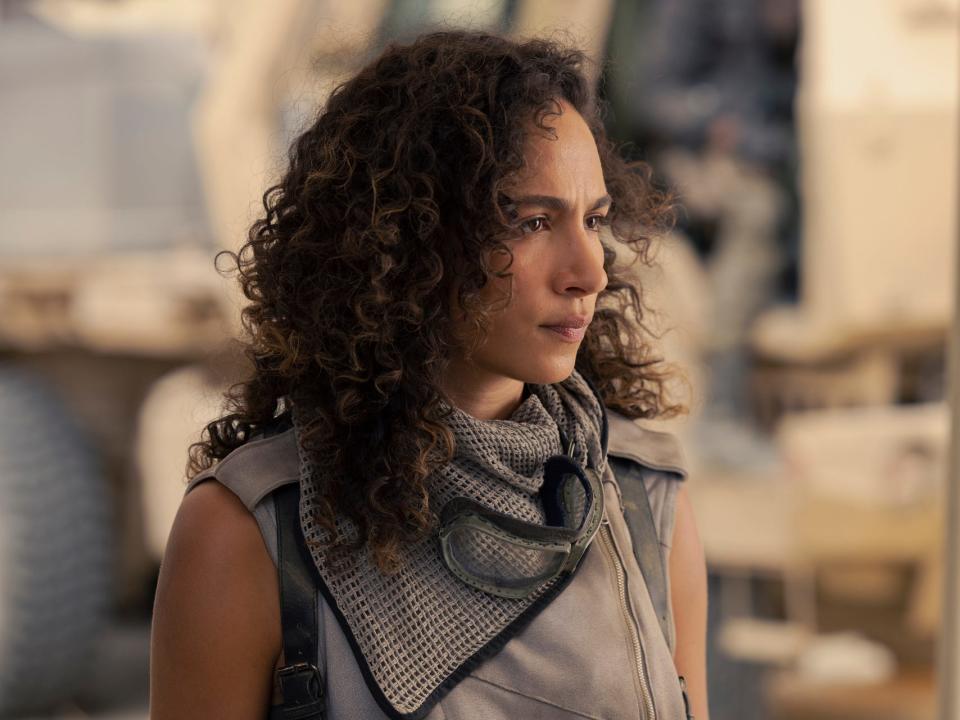 A woman in her late 20s wearing a gray sleeves top and with curly brown hair stares intently off camera.