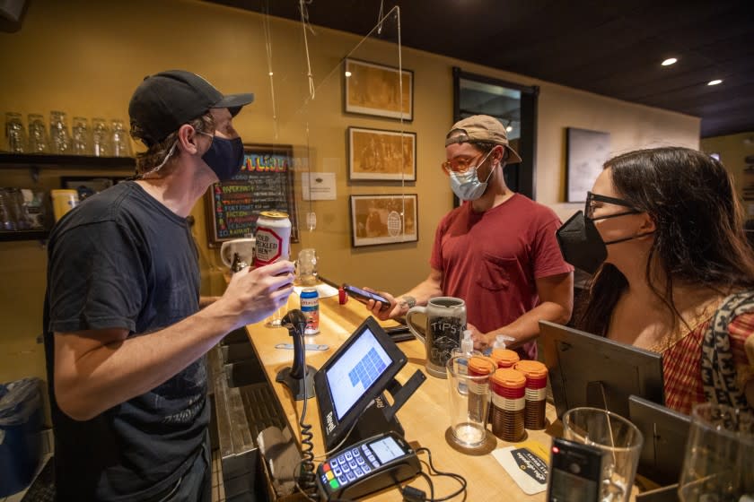 LOS ANGELES, CA - AUGUST 10: Bennett Erickson, left, general manager at Sunset Beer checks proof of vaccination for Anthony Trapanese, middle, and Caitlin Forst, right, on Tuesday, Aug. 10, 2021 in the Echo Park neighborhood of Los Angeles, CA. Los Angeles County required to show proof of vaccination before entering. The report will consider whether a mandate should require one dose or full vaccination to enter certain locations, and whether the policy should apply to all indoor public spaces or certain nonessential businesses and events. (Francine Orr / Los Angeles Times)