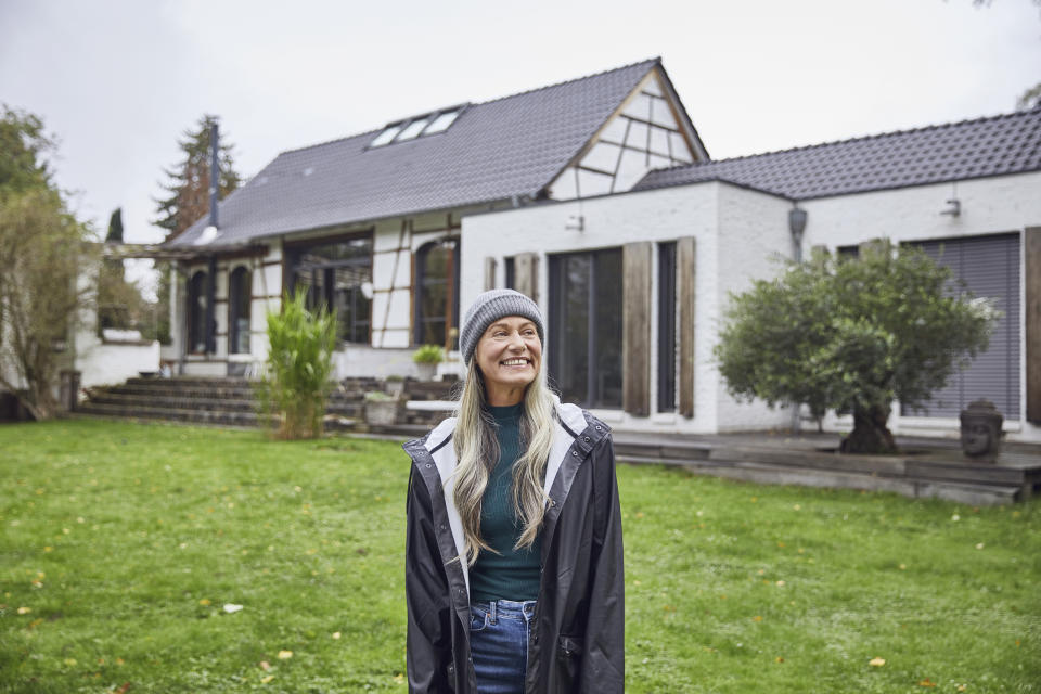 A woman smiling in front of her house