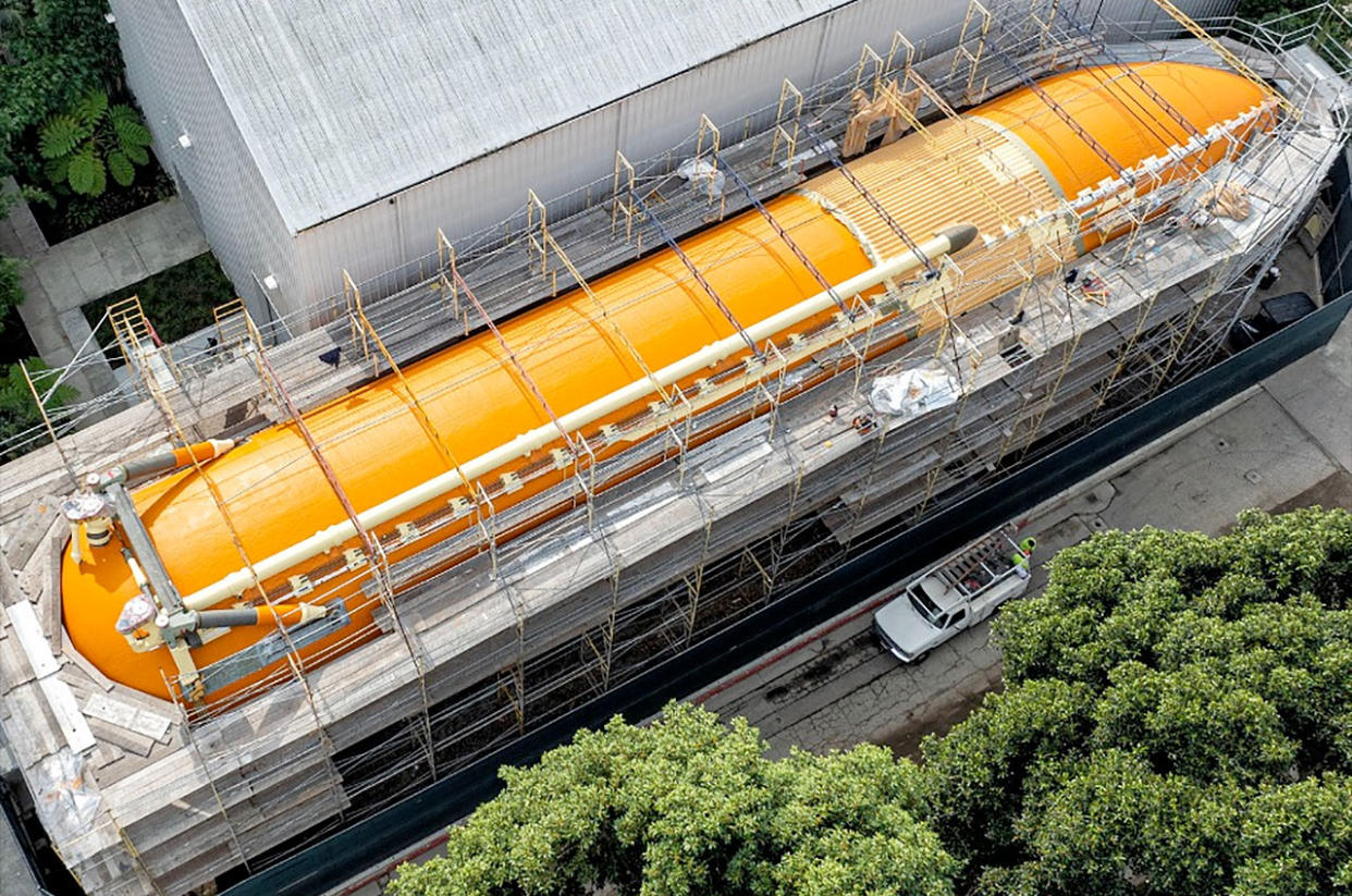  A space shuttle's orange external fuel tank is surrounded by scaffolding and fencing. 