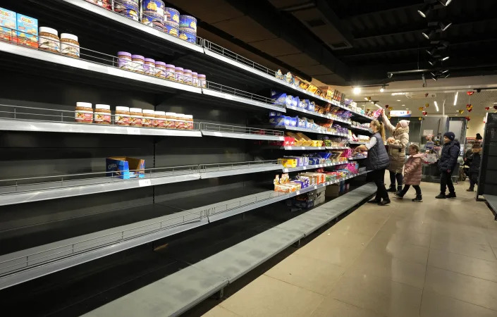 People select items from shelves at a shop. Half of the shelves are empty.