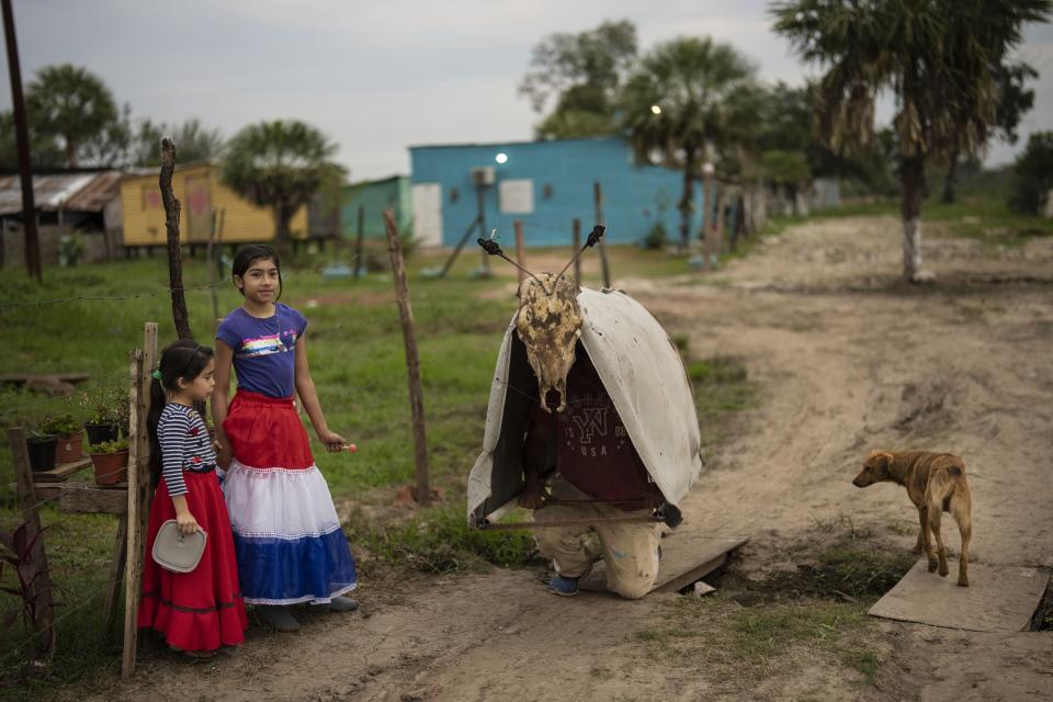 Sofía Maldonado, vestida con una falda con los colores nacionales, junto a su padre vestido como "Toro Kandil" para las fiestas de San Juan, en el barrio Kuna Pyapy Mbarete, en las afueras de Asunción, Paraguay, el 6 de julio de 2024. (Foto AP/Rodrigo Abd)