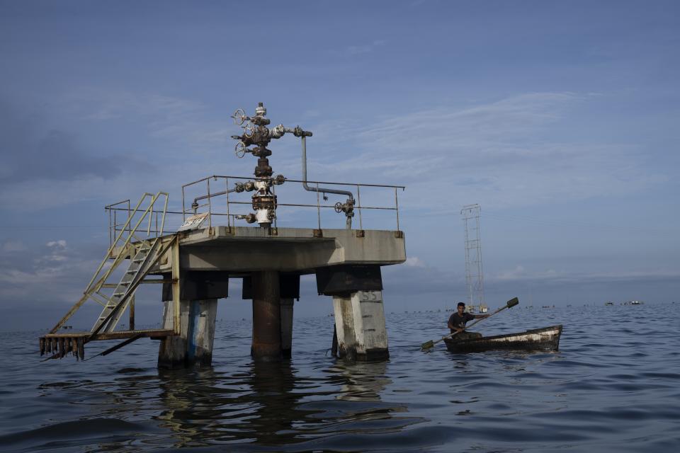 FILE - A fisherman navigates past an inoperative oil drill on Lake Maracaibo in Venezuela, early Oct. 12, 2022.A 49-page indictment unsealed on Oct. 20 in New York federal court has charged seven individuals with conspiring to smuggle oil from PDVSA, purchase sensitive U.S. military technology, and launder tens of millions of dollars on behalf of wealthy Russian businessmen. (AP Photo/Ariana Cubillos, File)