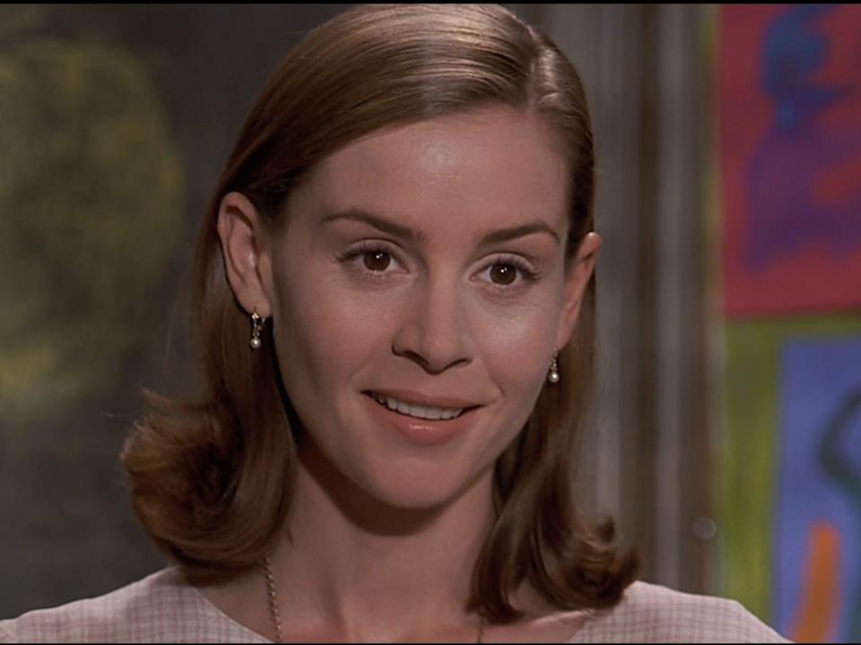 Embeth Davidtz as Miss Honey with pearl drop earrings and a pink dress in a classroom