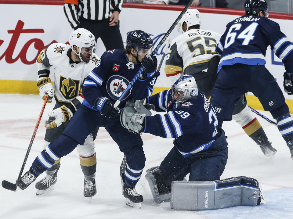 Winnipeg Jets goaltender Laurent Brossoit (39) saves the shot as Morgan Barron (36) defends against Vegas Golden Knights' William Carrier (28) during the first period of an NHL hockey game in Winnipeg, Manitoba on Thursday, Oct. 19, 2023. (John Woods/The Canadian Press via AP)