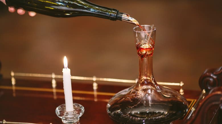 Pouring wine into a decanter over a candle