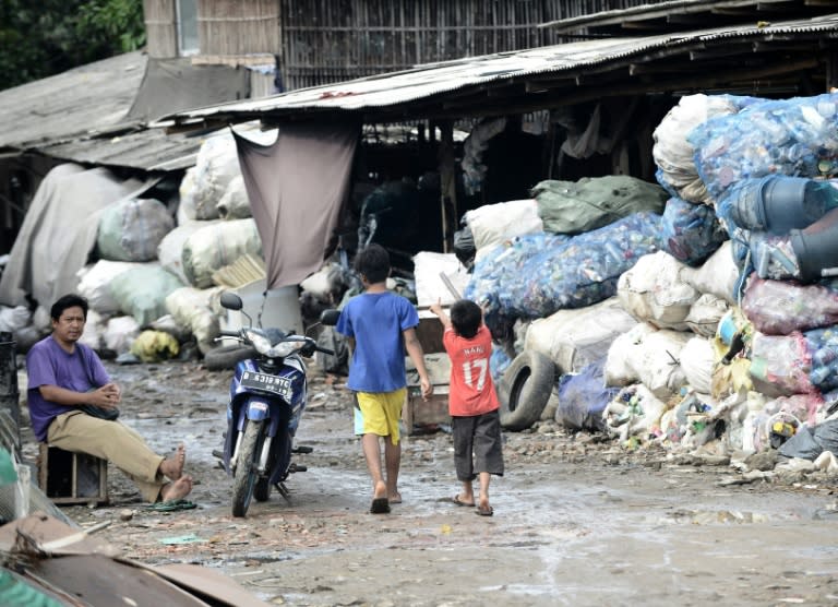 Two Indonesian kids walk pass bags of recyclable items collected by scavengers at a dumpsite in Jakarta