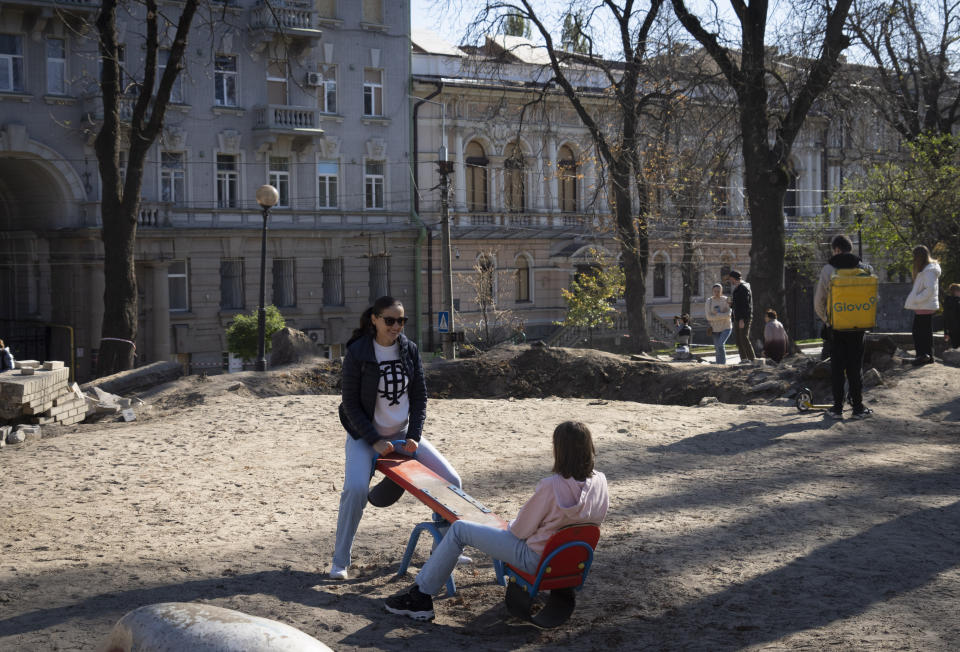 A mother and daughter play in a playground near a huge crater left by a Russian rocket a week ago, in central Kyiv, Ukraine, Sunday, Oct. 16, 2022. Ukrainians' resilience in the nearly 8-month-old war continues to be unwavering, despite an uptick in attacks that are seen as Russian President Vladimir Putin's vengeful response to an explosion that damaged a Moscow-built bridge to the Kremlin-annexed Crimean Peninsula on Oct. 8. (AP Photo/Efrem Lukatsky)