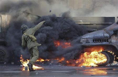 A protester throws stones as a vehicle is on fire during clashes with anti-government protesters in Kiev February 18, 2014. REUTERS/Konstantin Chernichkin