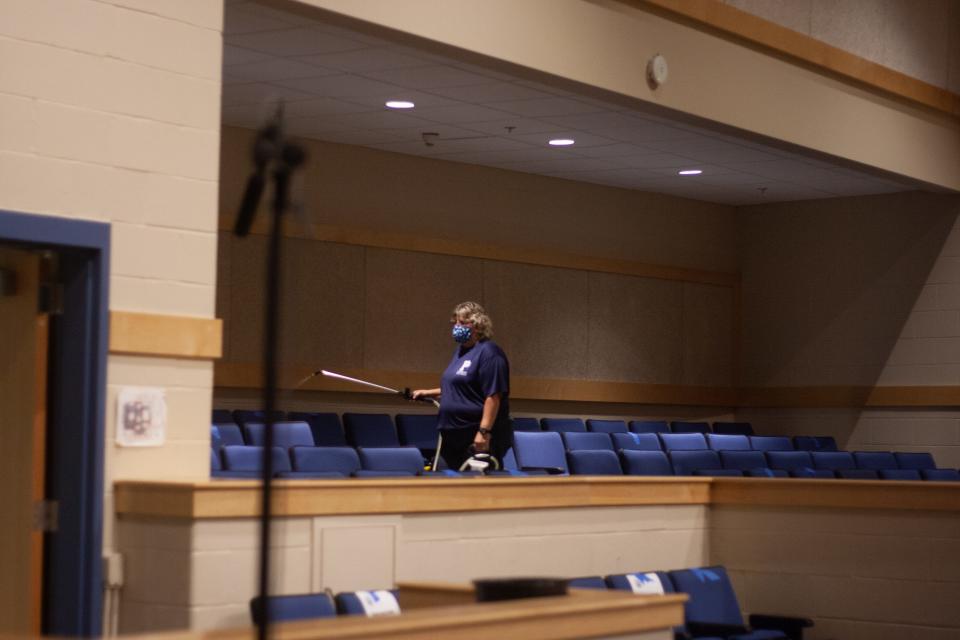 A woman sprays sanitizer over chairs in the Pembroke High School auditorium, July 28, 2020, following the annual town meeting.