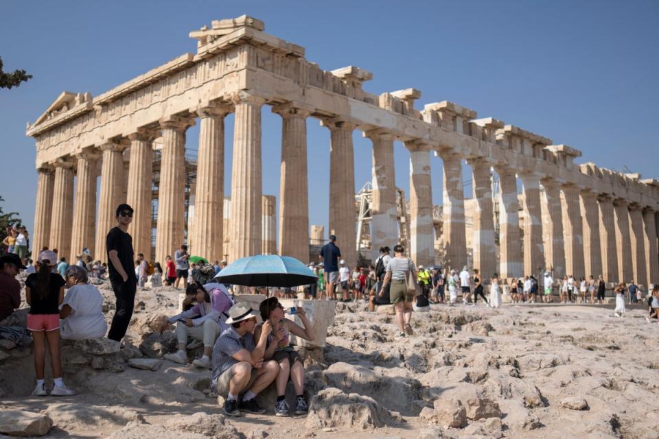 Una turista beve acqua mentre lei e un uomo si siedono sotto l'ombrellone davanti al tempio del Partenone risalente al V secolo a.C. sulla collina dell'Acropoli durante un'ondata di caldo (AP)