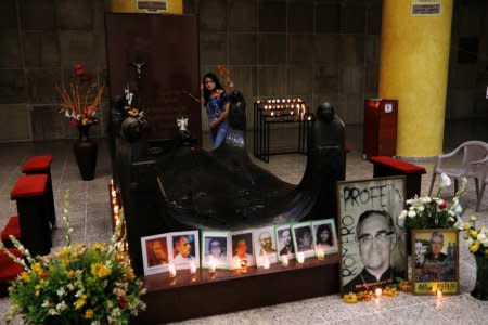 A woman walks by the grave of slain Salvadorean Archbishop Oscar Arnulfo Romero as pictures of him and other murdered priests are displayed during a vigil to await the announcement of his canonization date, in San Salvador, El Salvador on May 19, 2018.REUTERS/Jose Cabezas