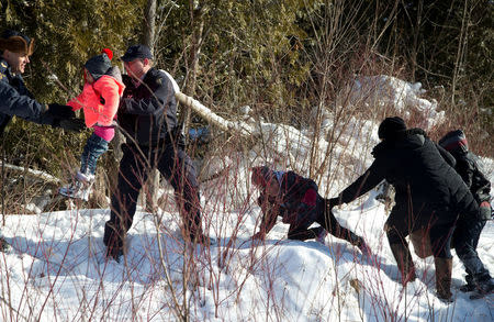 Royal Canadian Mounted Police (RCMP) officers assist a child from a family that claimed to be from Sudan as they walk across the U.S.-Canada border into Hemmingford, Canada, from Champlain in New York. REUTERS/Christinne Muschi