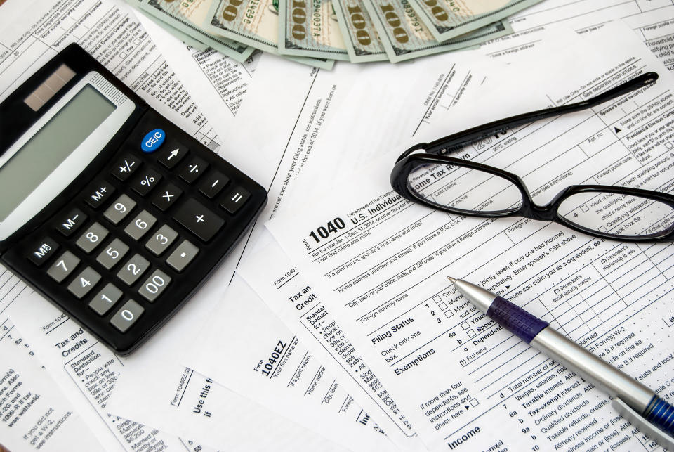 Calculator, pen, glasses, and money with tax forms.