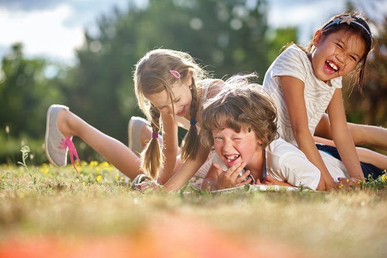 Three children laughing in a bundle on some grass