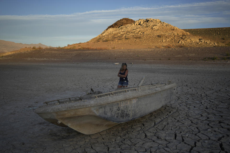 Misha McBride looks at a formally sunken boat now on cracked earth hundreds of feet from what is now the shoreline on Lake Mead at the Lake Mead National Recreation Area, Monday, May 9, 2022, near Boulder City, Nev. (AP Photo/John Locher)