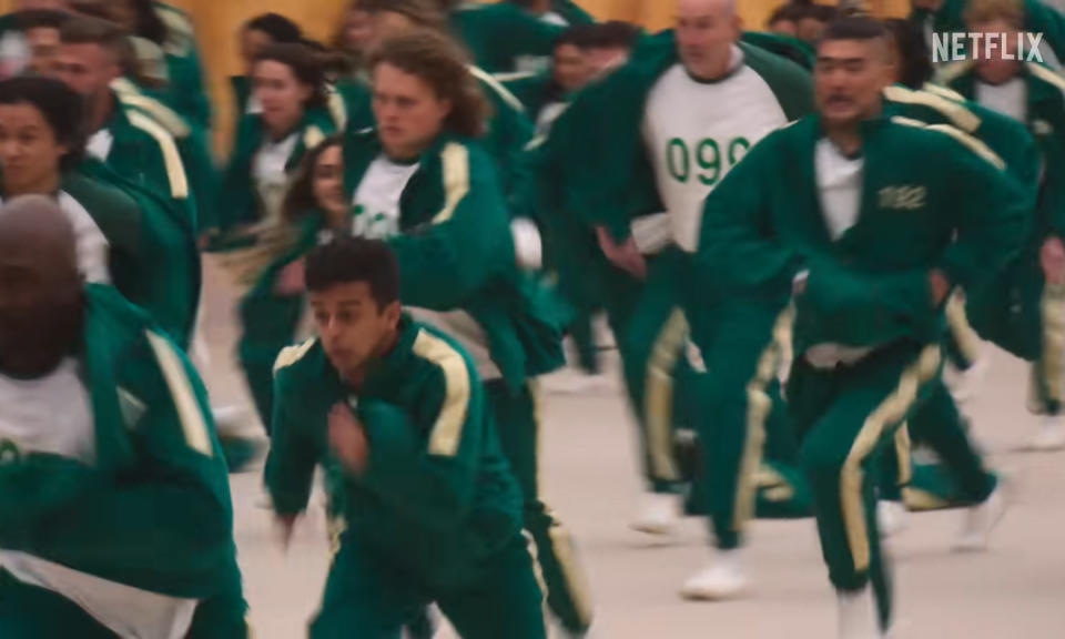 Teilnehmer in grünen Trainingsanzügen sprinten über eine Halle.