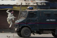 A masked Kashmiri protester jumps on an Indian police armored vehicle as he throws stones at it during a protest in Srinagar on May 31, 2019. (AP Photo/Dar Yasin)