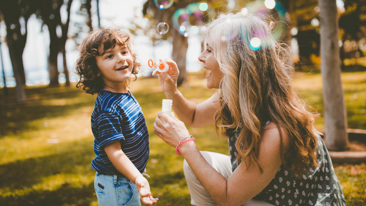 Beautiful grandmother playing and having fun blowing bubbles with grandson in the park.