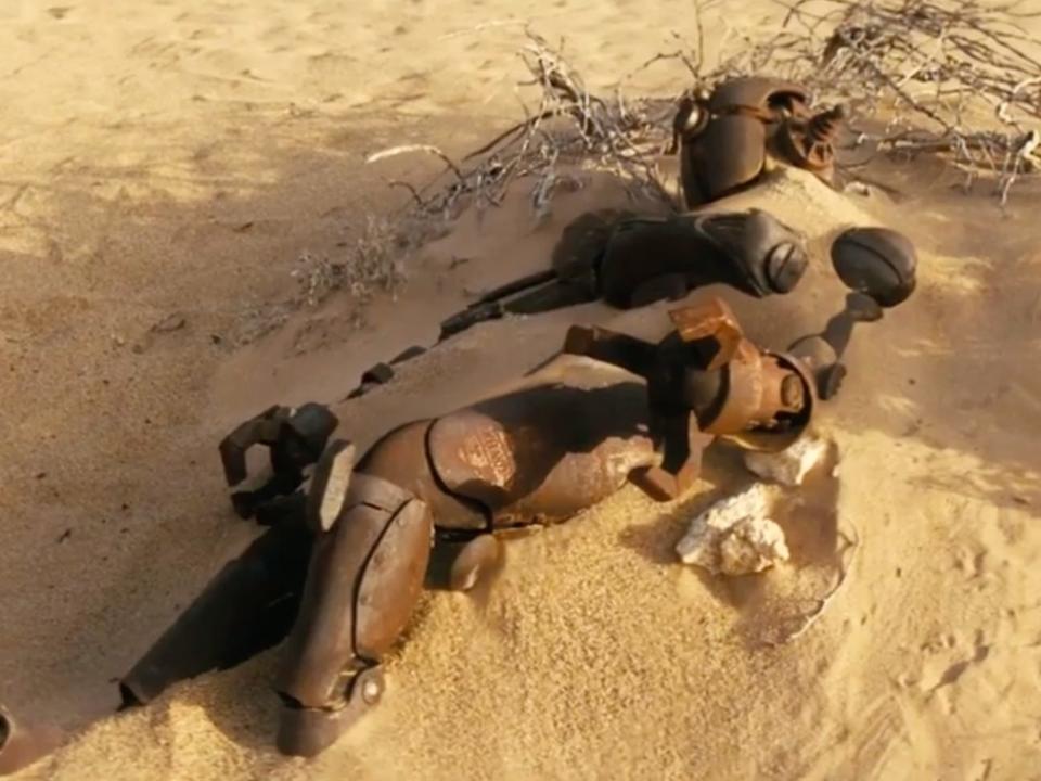 A broken Assaultron robot buried in the sand in "Fallout."