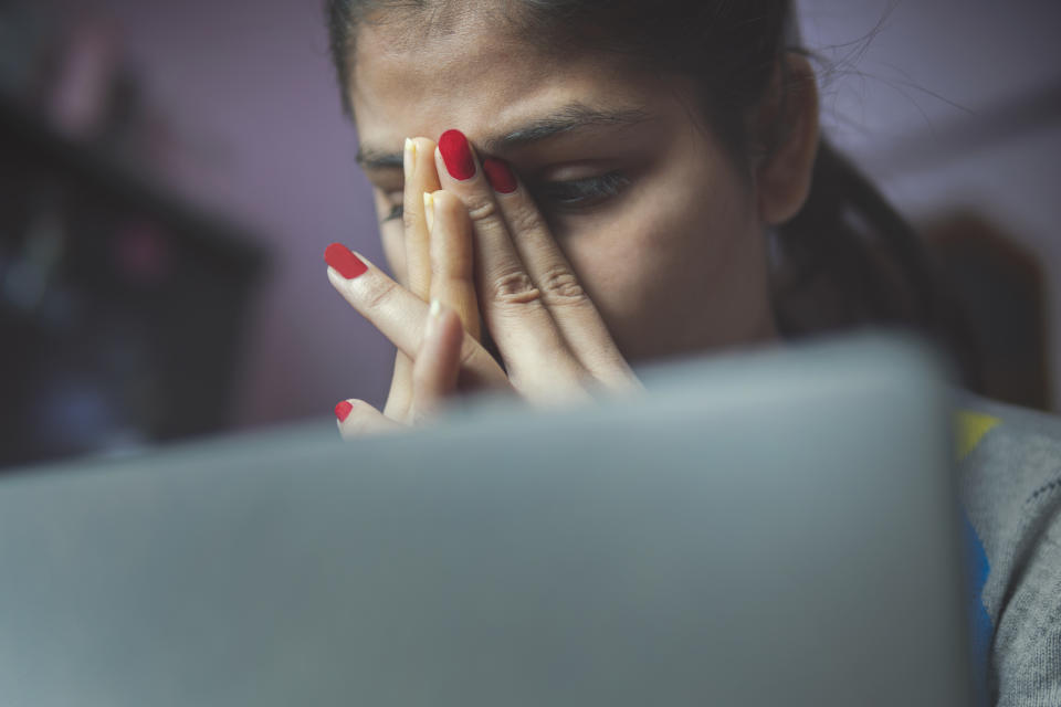 Indoor low angle image of a tensed worried young woman feeling tired during working on the laptop at home.