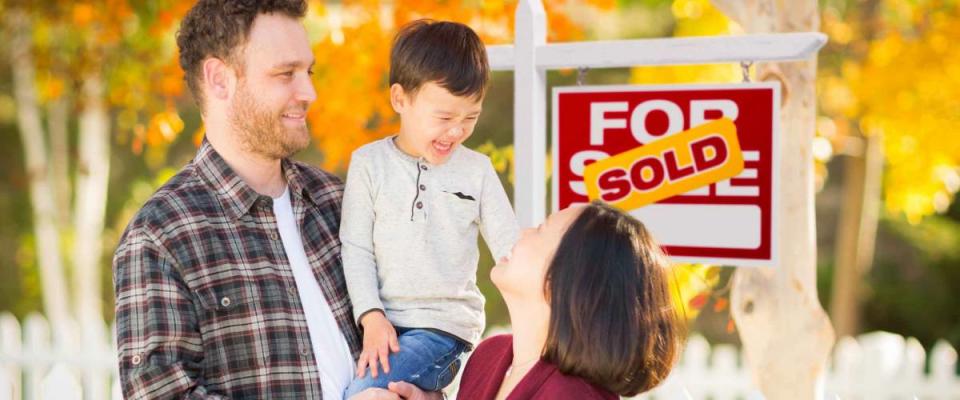 Young Mixed Race Chinese and Caucasian Family In Front of Sold For Sale Real Estate Sign and Fall Yard.