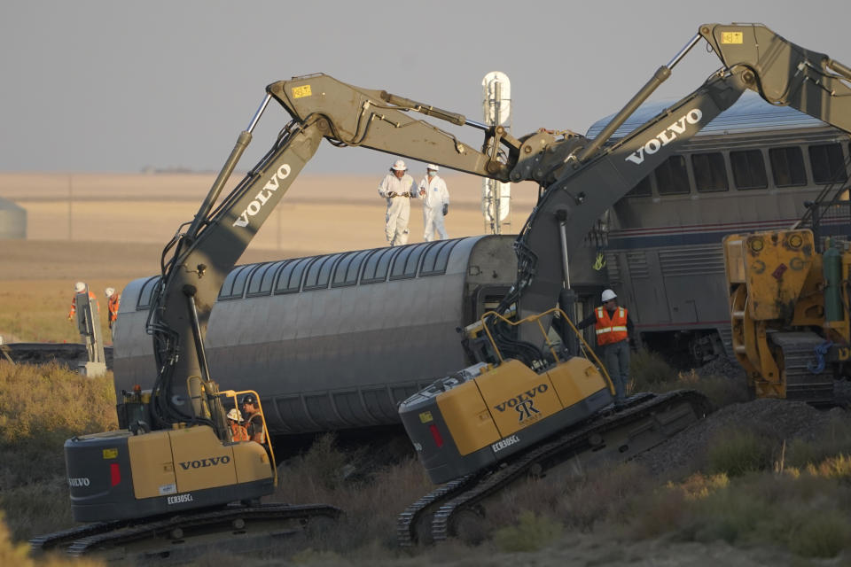 FILE - Workers stand on a train car on its side as front-loaders prop up another train car, Sept. 26, 2021, from an Amtrak train that derailed the day prior just west of Joplin, Mont., killing three people and injuring 49 others. The westbound Empire Builder was en route to Seattle from Chicago with two locomotives and 10 cars when it derailed. The derailment was caused by a combination of track issues, including wear and railbed instability, the National Transportation Safety Board said on Thursday, July 27, 2023. (AP Photo/Ted S. Warren, File)