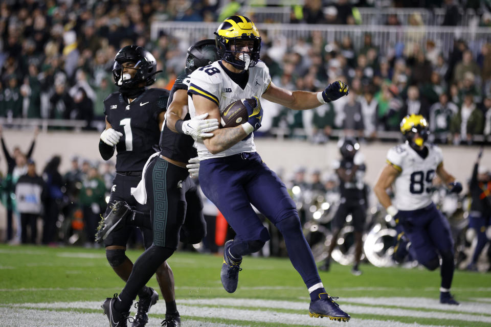 Michigan tight end Colston Loveland (18) scores a touchdown against Michigan State defensive backs Jaden Mangham (1) and Dillon Tatum, second from left, during the first half of an NCAA college football game, Saturday, Oct. 21, 2023, in East Lansing, Mich. (AP Photo/Al Goldis)