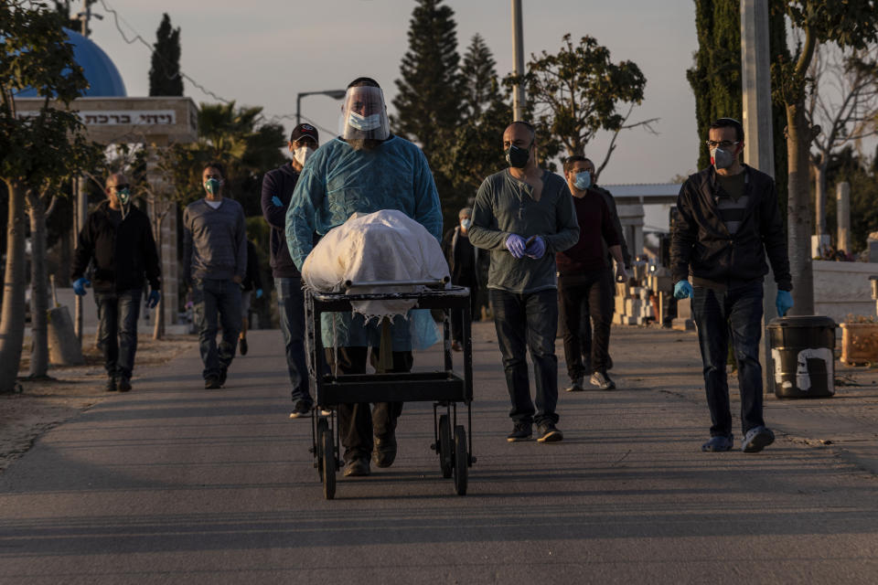 Member of Hevra Kadisha, an organization which prepares bodies of deceased Jews for burial according to Jewish tradition, pushes a body during a funeral of a Jewish man who died from coronavirus in the costal city of Ashkelon, Israel, Thursday, April 2, 2020. (AP Photo/Tsafrir Abayov)