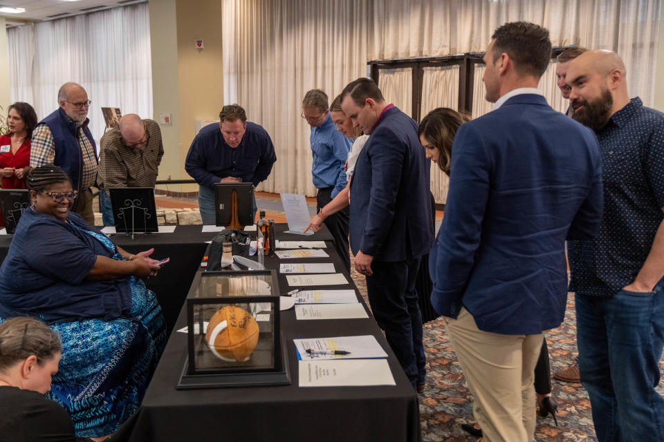 Attendees look over silent auction items that include a Dallas Cowboys signed football Tuesday at the Heroes and Legends fundraiser event at the Amarillo Civic Center.