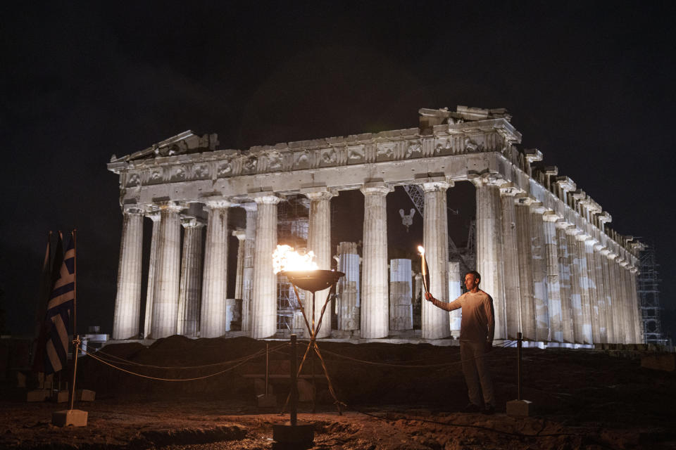 Retired Greek 400-meter hurdles champion Periklis Iakovakis holds a torch after he lit a cauldron with the Olympic flame in front of the ancient Parthenon temple at the Acropolis hill on Friday, April 19, 2024. The flame that will burn at the summer Olympics is spending the night at the ancient Acropolis in Athens, a week before its handover to Paris 2024 organizers. (AP Photo/Petros Giannakouris)