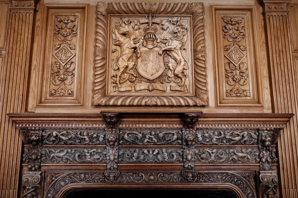 A fireplace flanked by warriors bearing an oak mantel. This is the only item in the castle retrieved from the original structure and dates back to the 1830s. A new chimneypiece carved with Queen Victoria's coat of arms was placed above the mantel and Edward VII's initials are also carved on either side