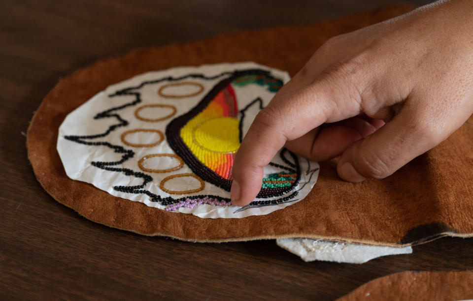 <em>Tendoy points to sprigs of lavender and sage her daughter designed for her son’s moccasins. Tendoy says her daughter picked out the colors of the design before she died. Tendoy is following all of her daughter’s instruction for the artwork. (Photo/Ava Rosvold | BYLINE magazine)</em>