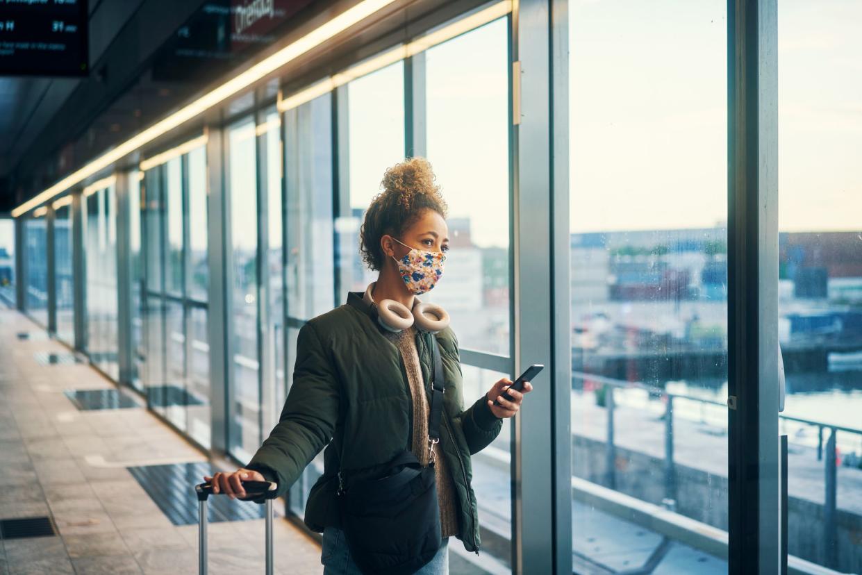 Shot of a masked young woman using a smartphone while travelling through a subway station