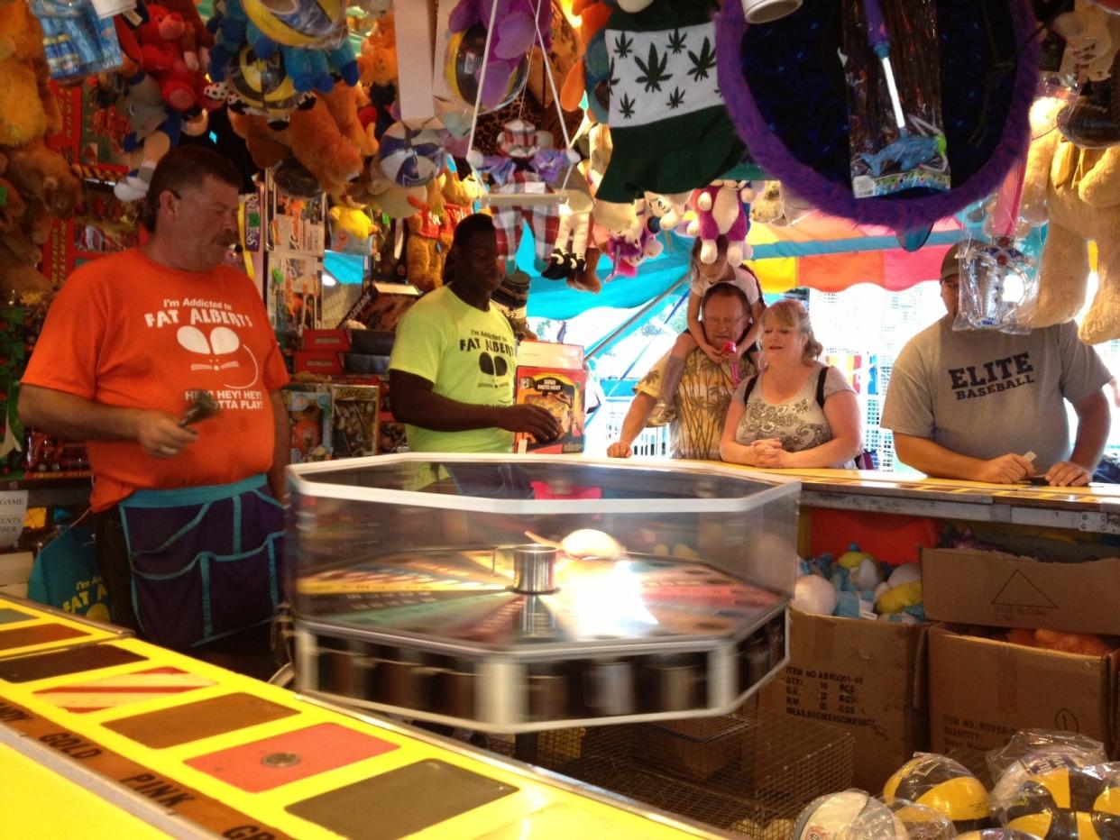From left to right, Brian and Brandon LaRew, father and son, manage a Cleveland County Fair booth with the game ‘Hey, Hey, Hey, It's Fat Albert.’ Albert scurries into a hole that players attempt to guess correctly to win prizes.
